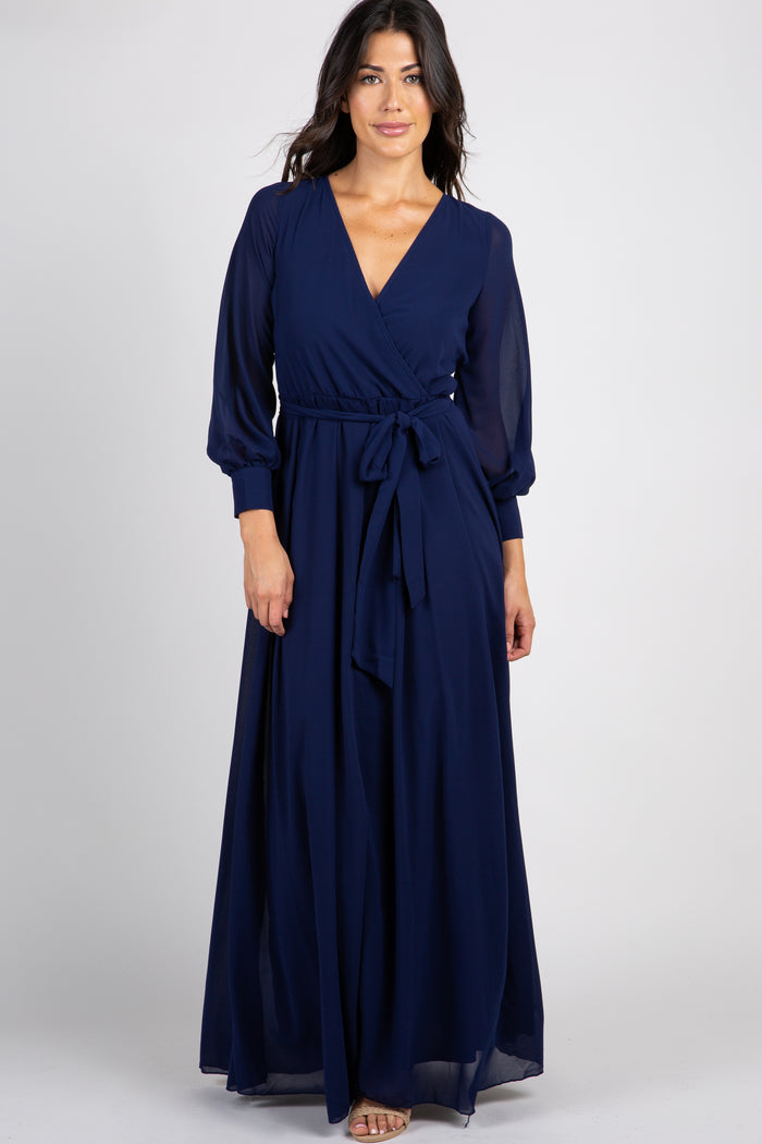 woman wearing a navy blue long sleeve wrap maxi dress with a waist tie against a white background