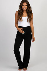 woman wearing a gray maternity vest over a dark sweater and black pants, holding her baby bump in front of a Christmas tree