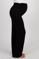 woman wearing a white maternity tank top and black maternity pants, holding her baby bump with a smile