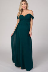 woman wearing a dark green off-the-shoulder maternity gown with a flowing skirt and ruched bodice, showcasing her baby bump