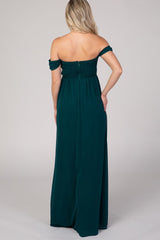 woman wearing a dark green off-the-shoulder maternity maxi dress with a smocked bodice and a flowing skirt