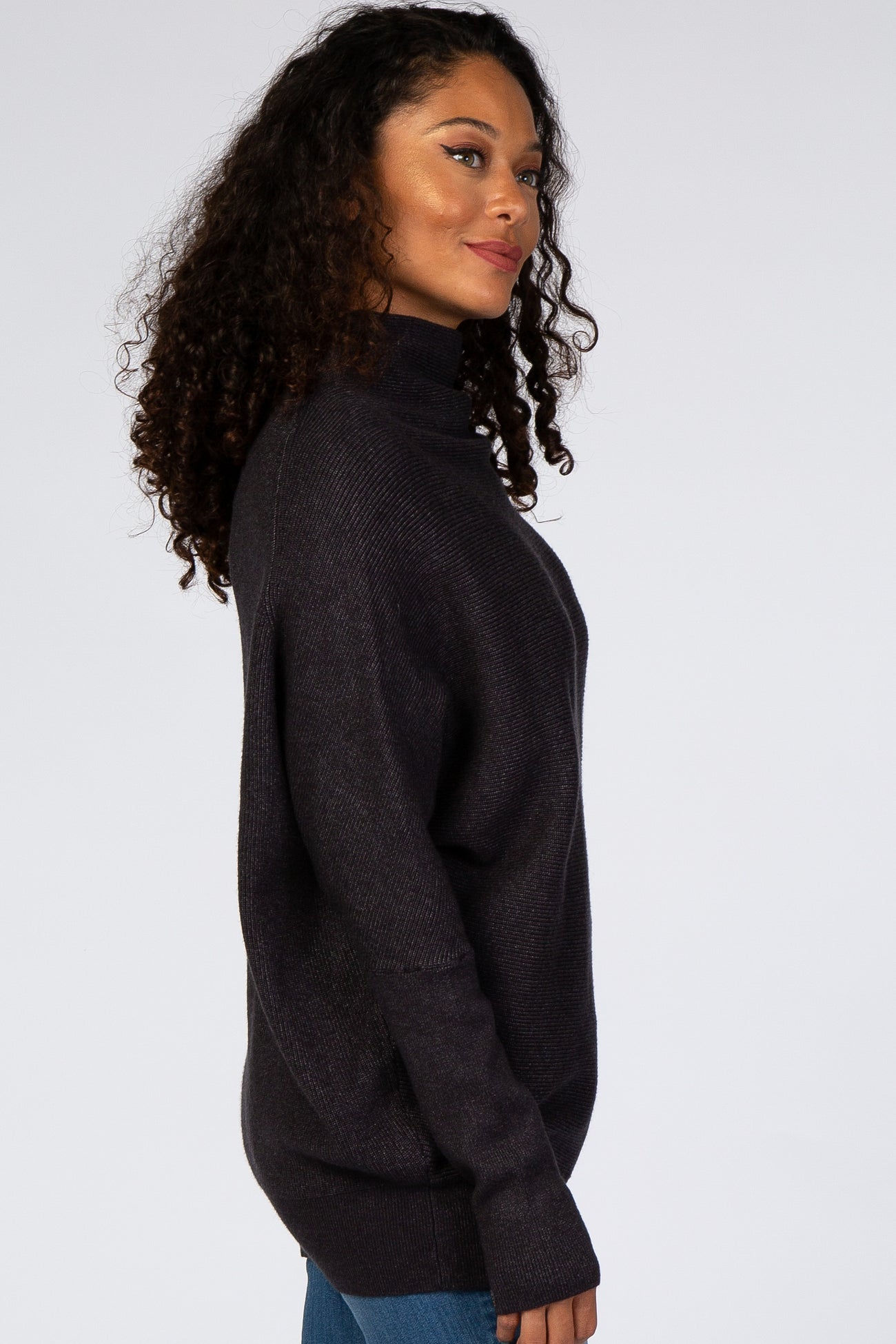 woman wearing a dark gray oversized turtleneck sweater with a relaxed fit and curly hair
