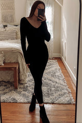 woman wearing a black long sleeve fitted dress and ankle boots, posing in front of a mirror in a cozy bedroom setting