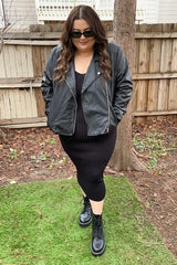 woman in black leather jacket, ribbed midi dress, and combat boots standing in a backyard