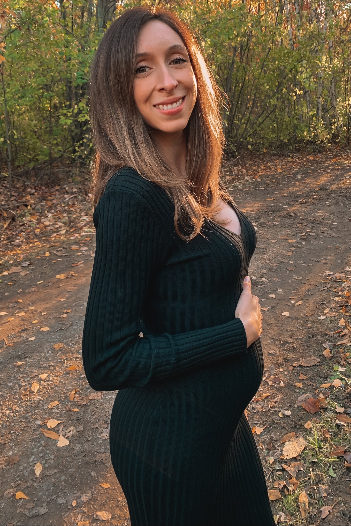 woman wearing a dark green ribbed maternity dress and holding her baby bump outdoors