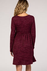 woman wearing a maroon long sleeve maternity dress with a gathered waist and a flowing skirt, showing the back view