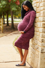 woman wearing a burgundy maternity dress with ruched details and a visible baby bump, leaning against a stone wall