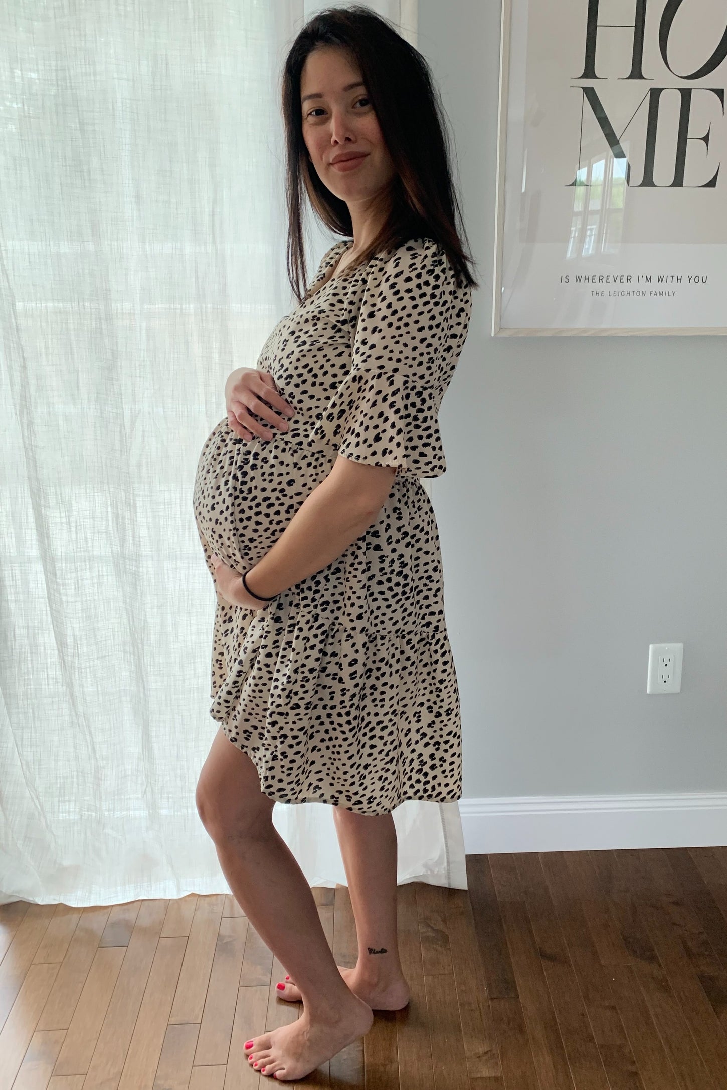 woman wearing a beige leopard print maternity dress and holding her baby bump