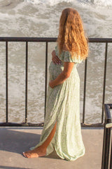 pregnant woman in floral maxi dress holding her baby bump while standing on a balcony overlooking the ocean
