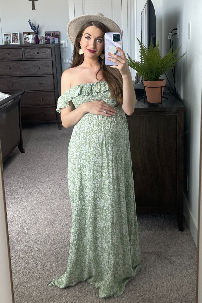 pregnant woman in green floral off-the-shoulder maternity maxi dress taking a mirror selfie