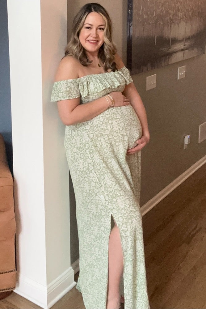 smiling pregnant woman in a green floral off-the-shoulder maternity dress holding her baby bump