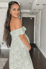 woman wearing a green floral off-shoulder maternity dress and holding her baby bump