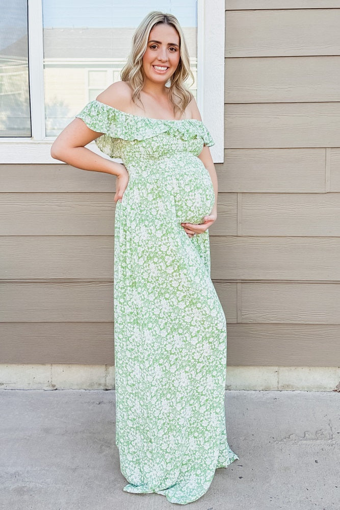 woman wearing a green floral off-the-shoulder maternity dress and cradling her baby bump