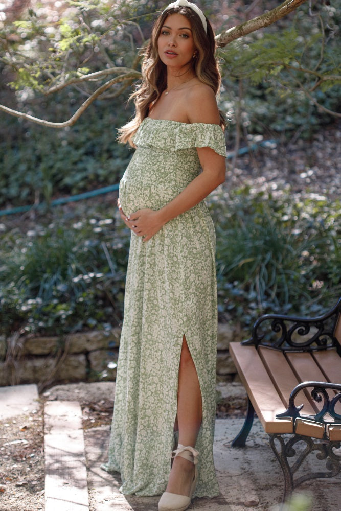 Pregnant woman in green floral off-the-shoulder maternity maxi dress posing outdoors near a park bench