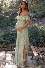 Pregnant woman in green floral off-the-shoulder maternity maxi dress posing outdoors near a park bench