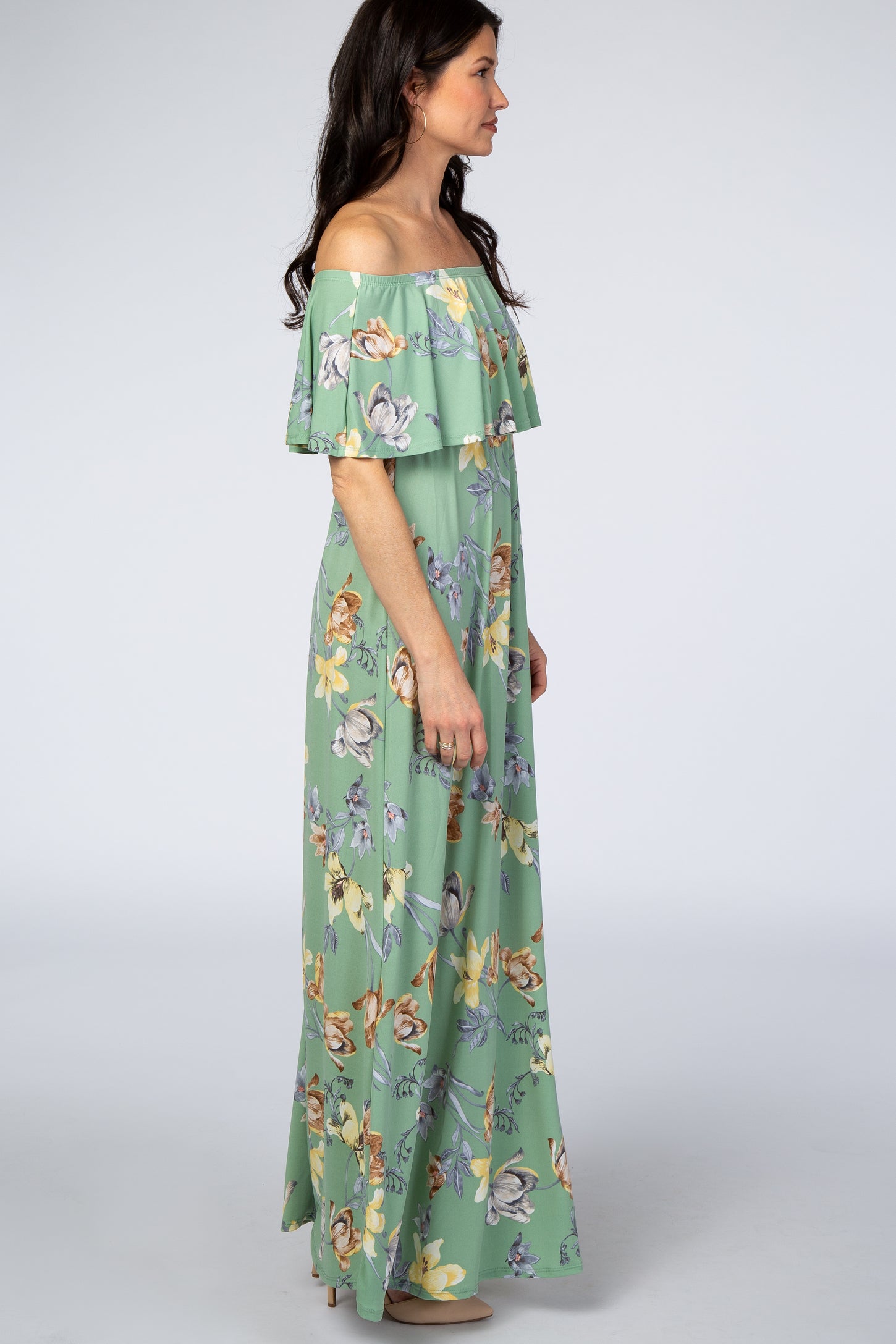 woman wearing a green off-the-shoulder floral maxi dress with ruffle detail, standing in profile