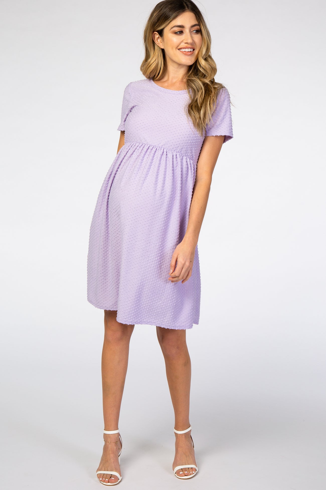 woman wearing a lavender short sleeve maternity dress with a textured pattern and a fitted waist, showing her baby bump
