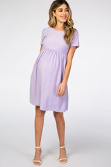 woman wearing a lavender short sleeve maternity dress with a textured pattern and a fitted waist, showing her baby bump