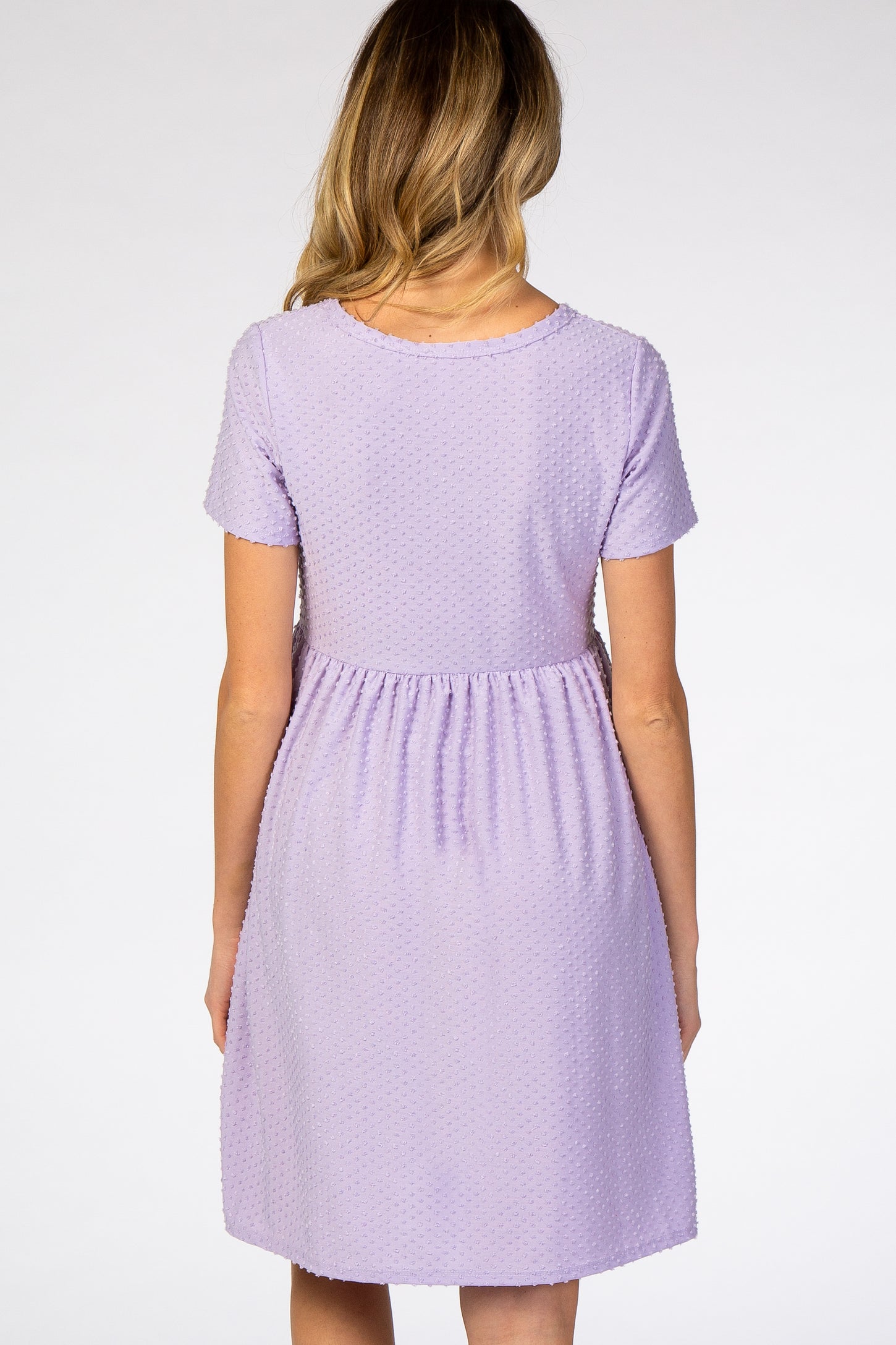 woman wearing a lavender short sleeve maternity dress with a textured dot pattern and a gathered waistline
