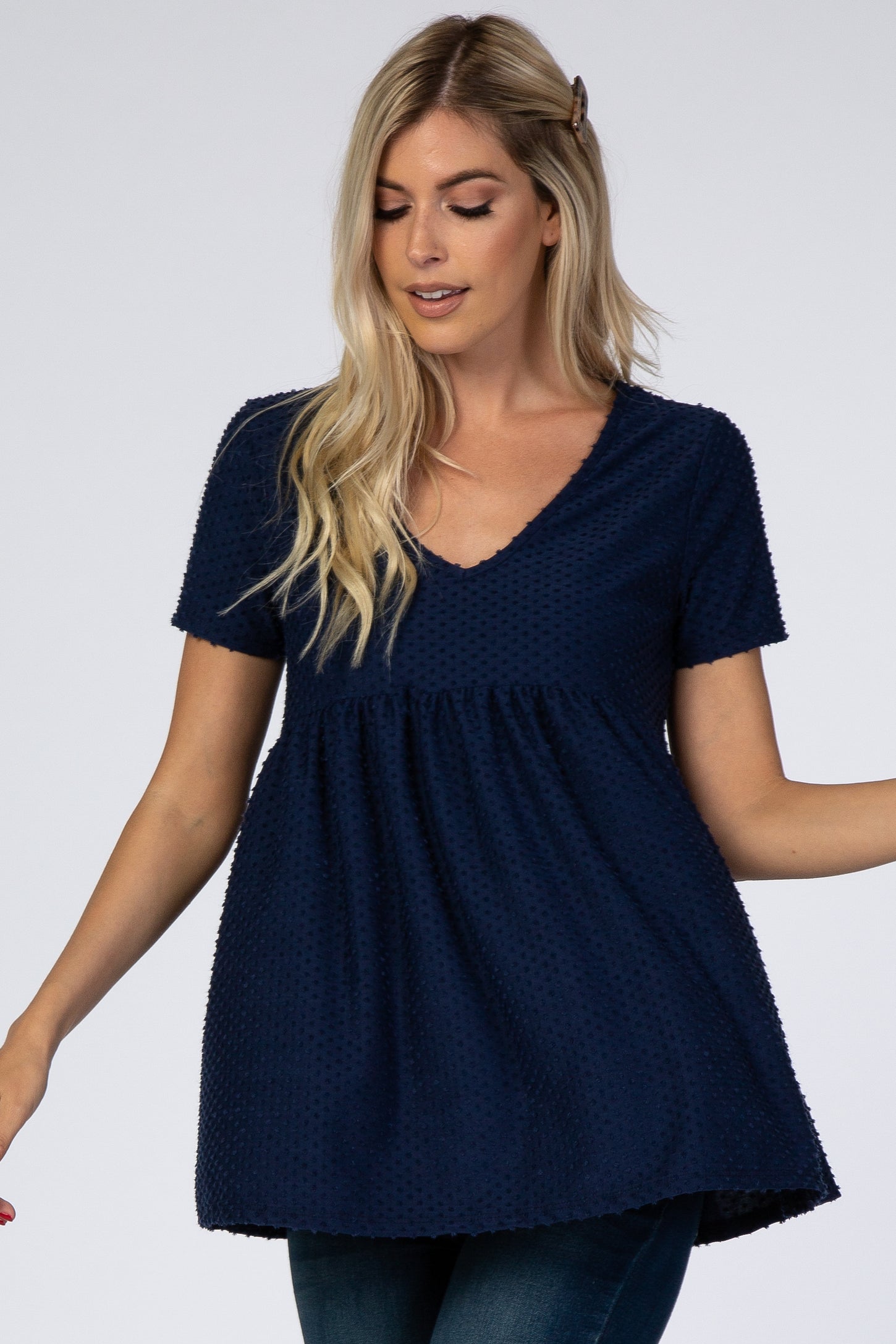 blonde woman wearing a navy blue short sleeve swiss dot maternity tunic top with a v-neckline