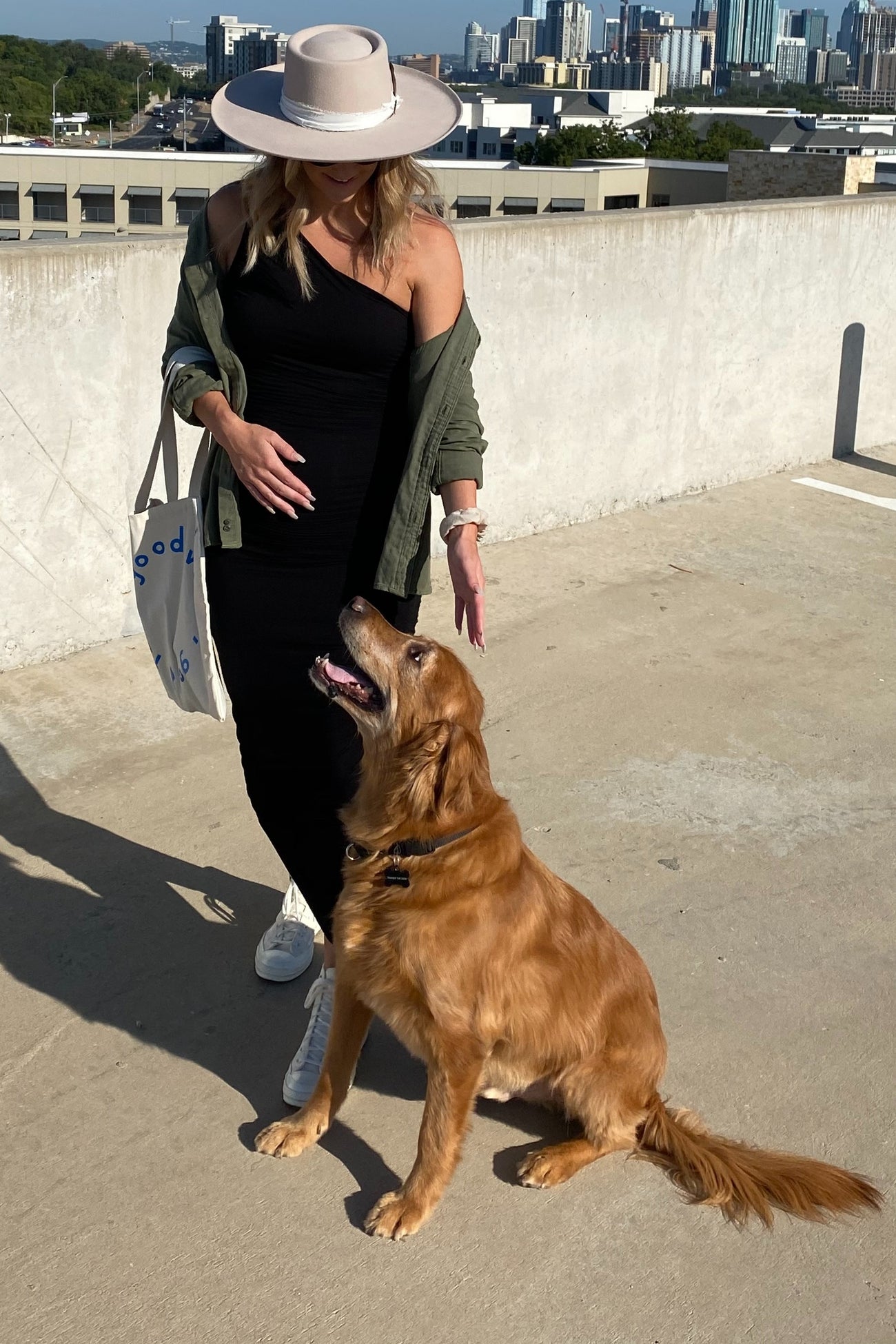 woman wearing a black maternity dress and green cardigan, standing with a golden retriever on a rooftop