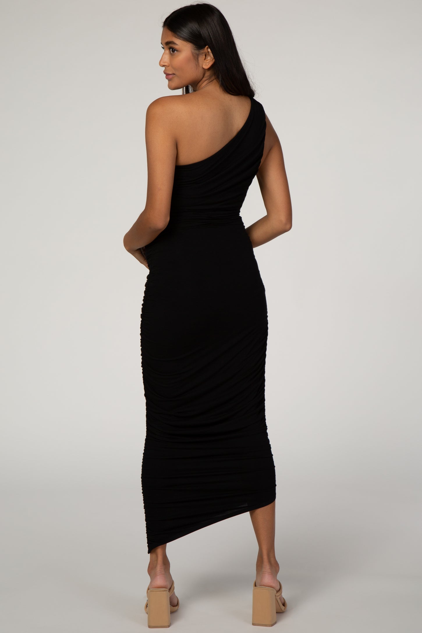 woman wearing a black one-shoulder maternity dress with ruching details and a mid-length hem, showcasing a baby bump