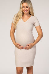 woman wearing a beige short sleeve maternity dress with a v-neck, cradling her baby bump