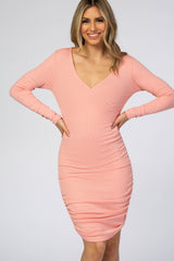 woman wearing a light pink long sleeve bodycon dress with a v-neck and ruching details on the sides