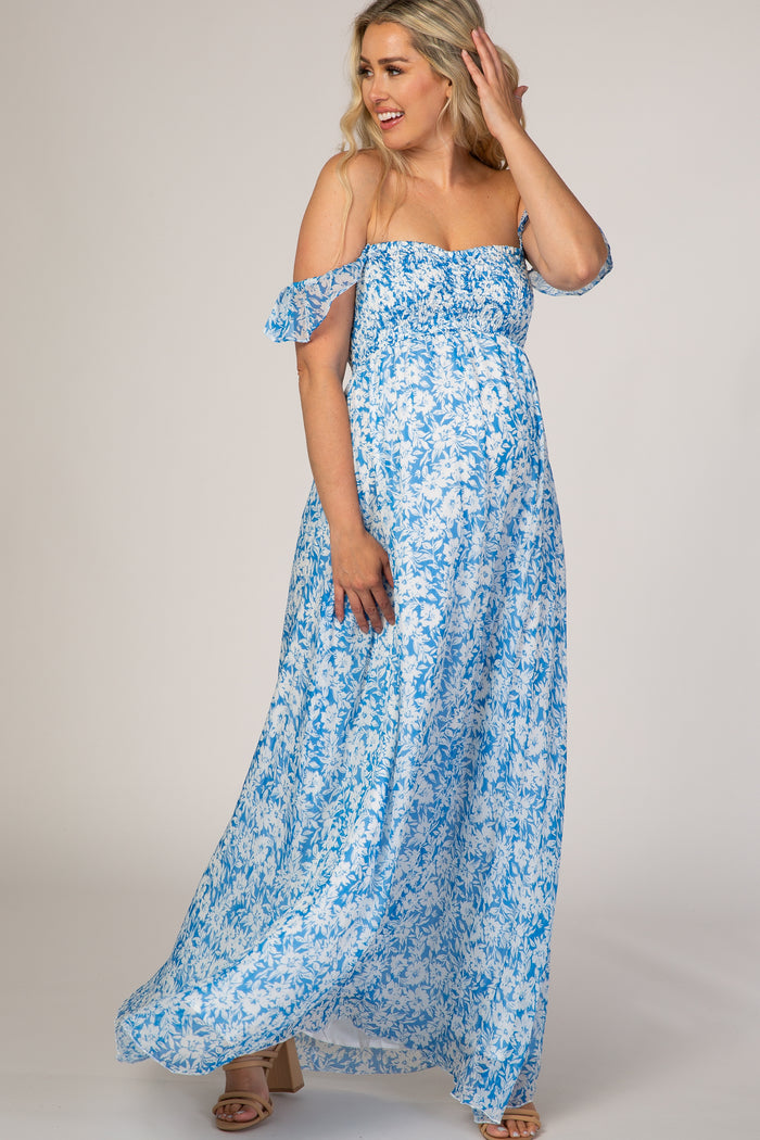 woman wearing a light blue floral off-shoulder maternity maxi dress with a smocked bodice and flowing skirt, baby bump visible