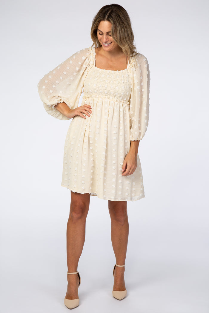 woman wearing a cream-colored dress with puff sleeves and a smocked bodice, standing and smiling