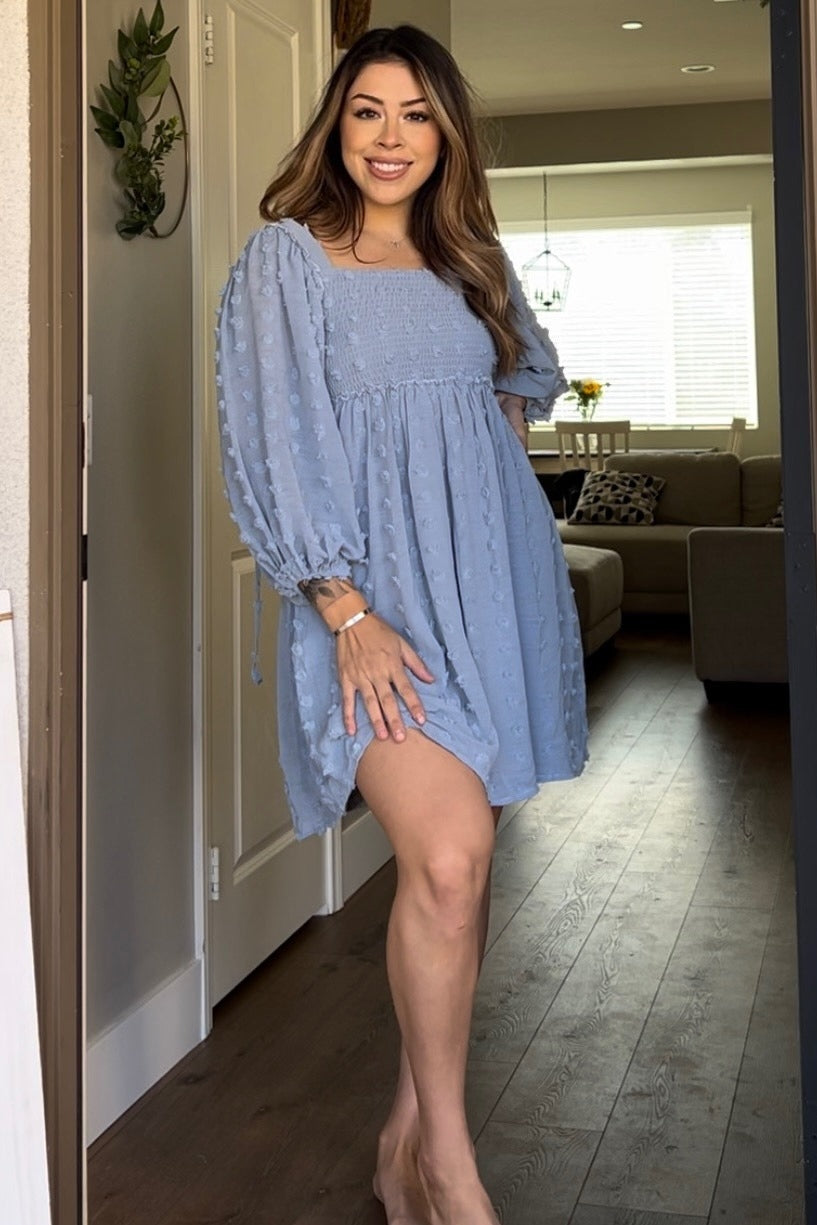 woman wearing a light blue smocked mini dress with puff sleeves standing in a doorway