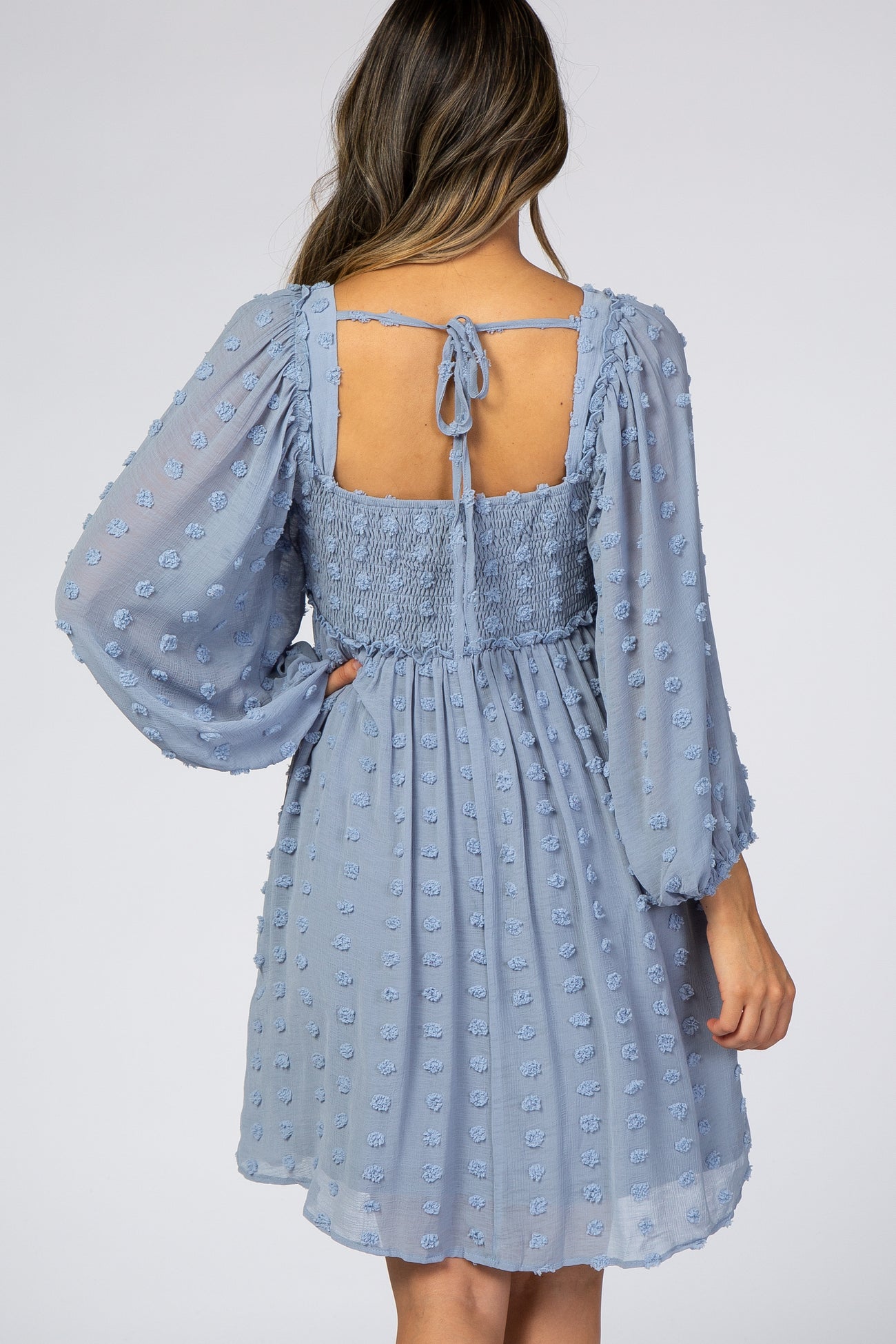 woman wearing a light blue short dress with puff sleeves and a smocked back, featuring textured floral details