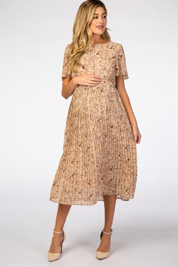 woman wearing a beige floral pleated maternity dress and gently holding her baby bump