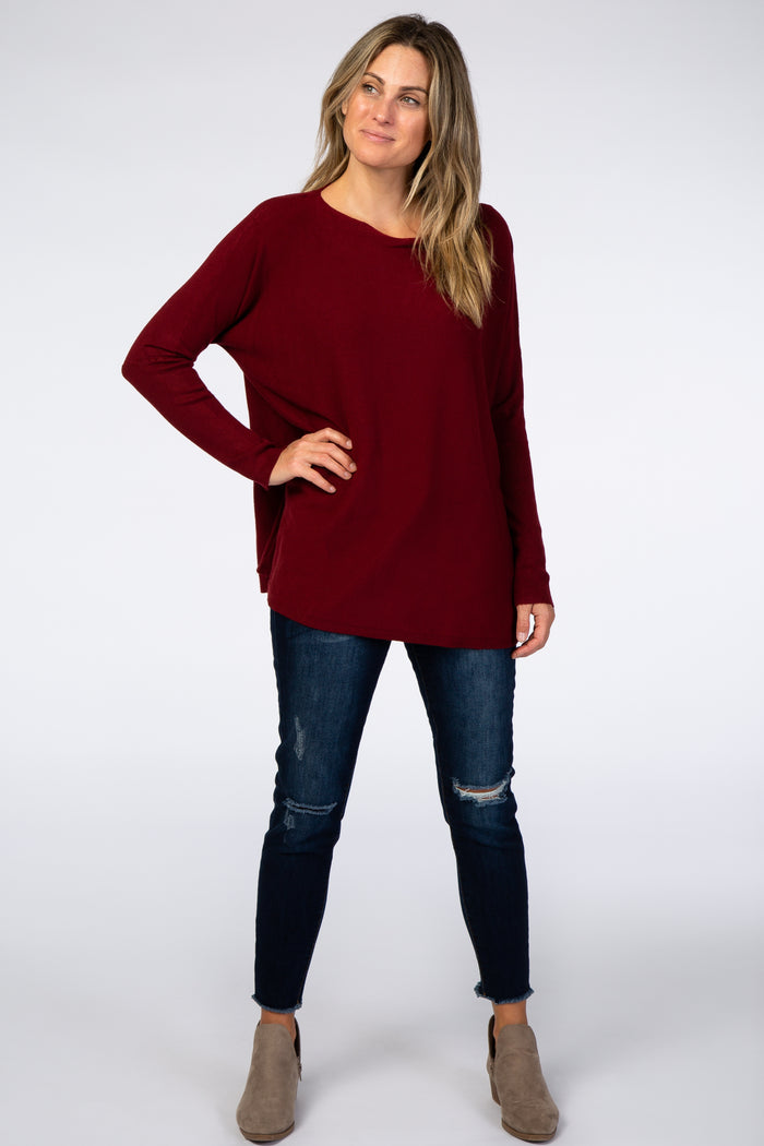 woman wearing a burgundy long sleeve top with a relaxed fit, paired with distressed dark jeans and ankle boots