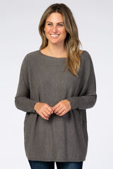 woman wearing a dark gray oversized sweater with a wide neckline and long sleeves, smiling at the camera