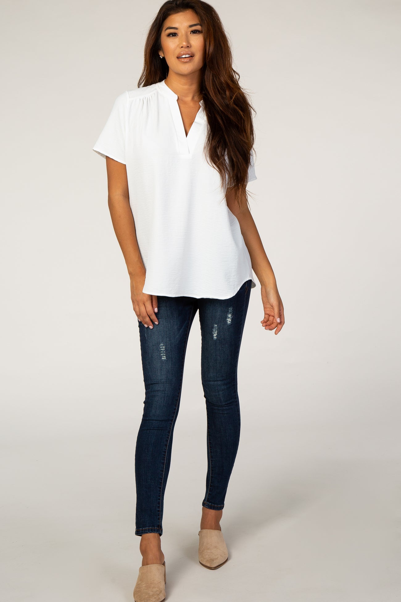 woman wearing a white short sleeve blouse with a v-neckline and blue skinny jeans