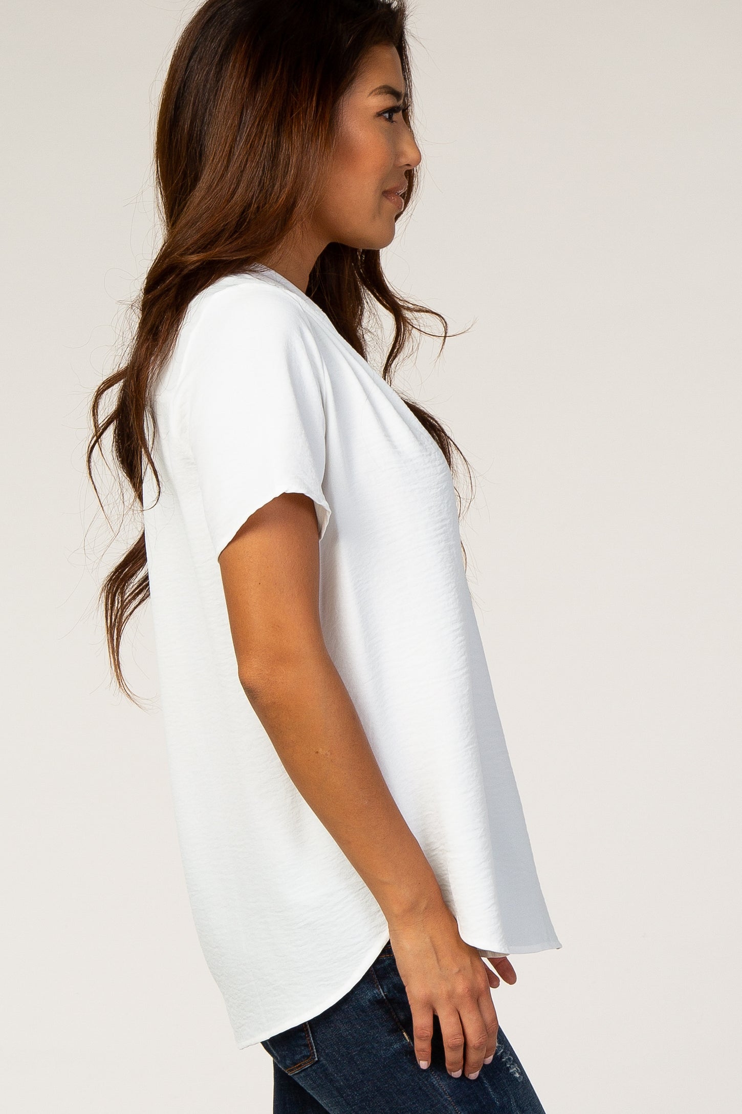 woman wearing a white short sleeve top with a relaxed fit and side slits, paired with dark wash jeans