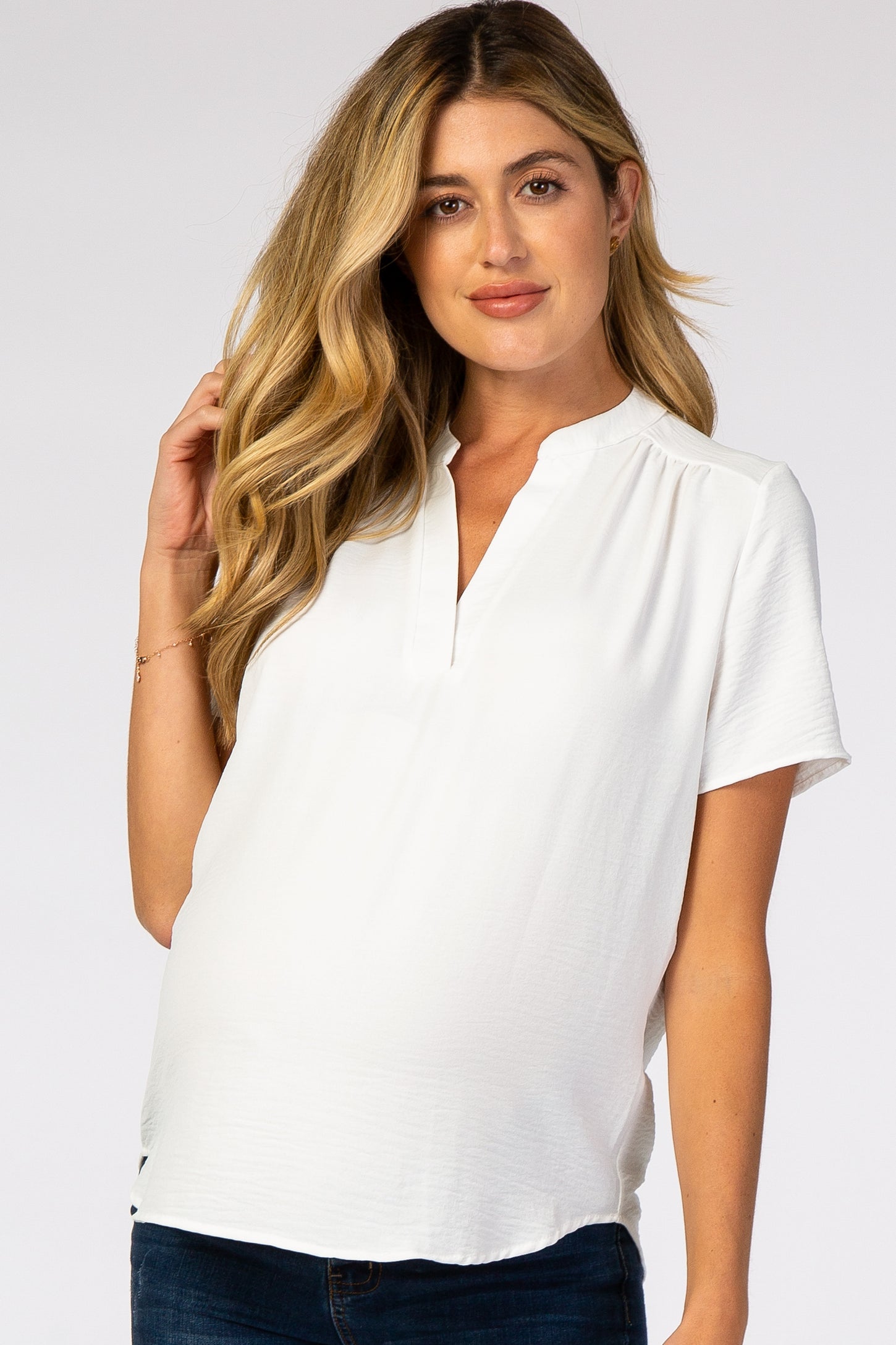 woman wearing a white short sleeve maternity top with a split neckline and visible baby bump