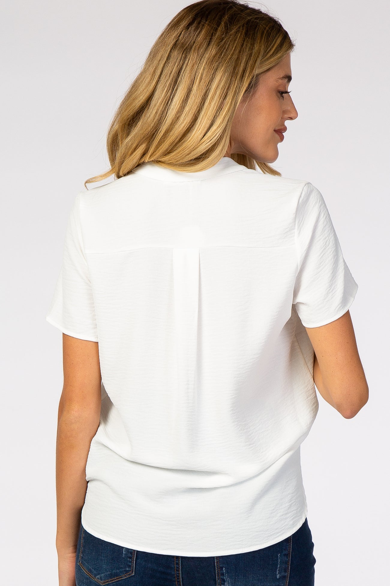 woman wearing a white short sleeve maternity top with a relaxed fit and back pleat detail
