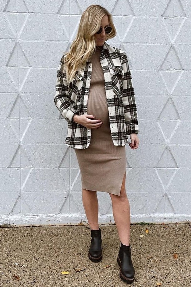 woman wearing a beige maternity dress with a plaid shacket and black ankle boots, showcasing her baby bump