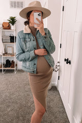 woman wearing a light blue denim maternity jacket over a brown ribbed maternity dress with a visible baby bump