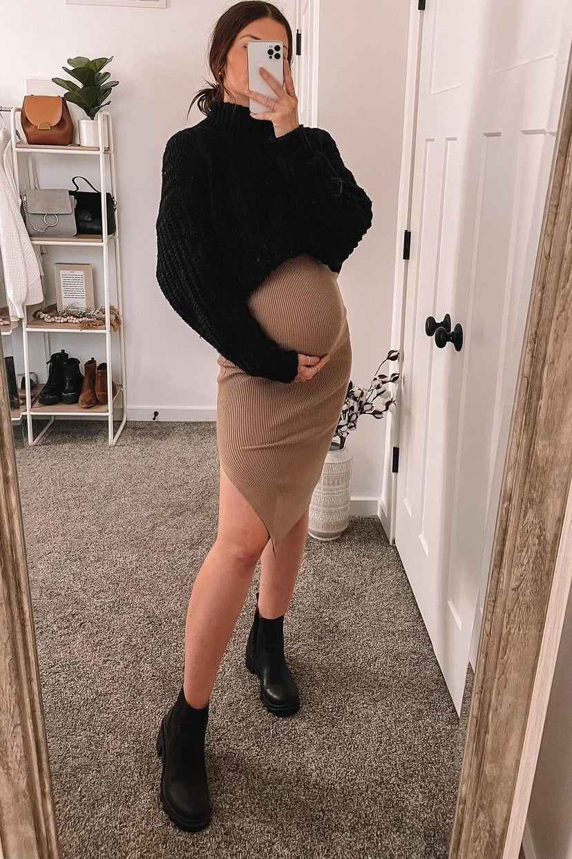 woman wearing a black oversized sweater and a beige form-fitting maternity dress, showing her baby bump