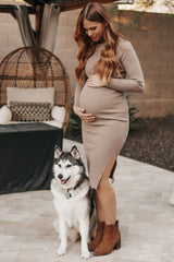 woman wearing a beige ribbed maternity dress with a side slit and holding her baby bump, standing next to a dog