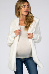 woman wearing a white fuzzy maternity cardigan over a light top, displaying her baby bump and styled with blue jeans