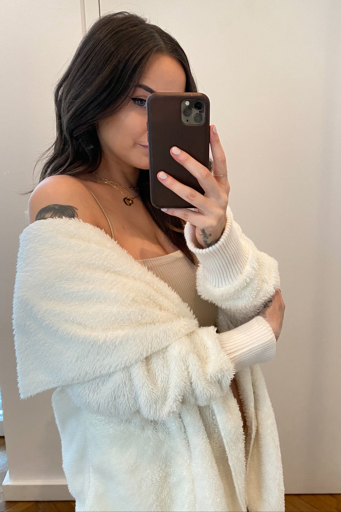 Woman taking mirror selfie wearing a white fuzzy cardigan and beige top