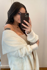 Woman taking mirror selfie wearing a white fuzzy cardigan and beige top