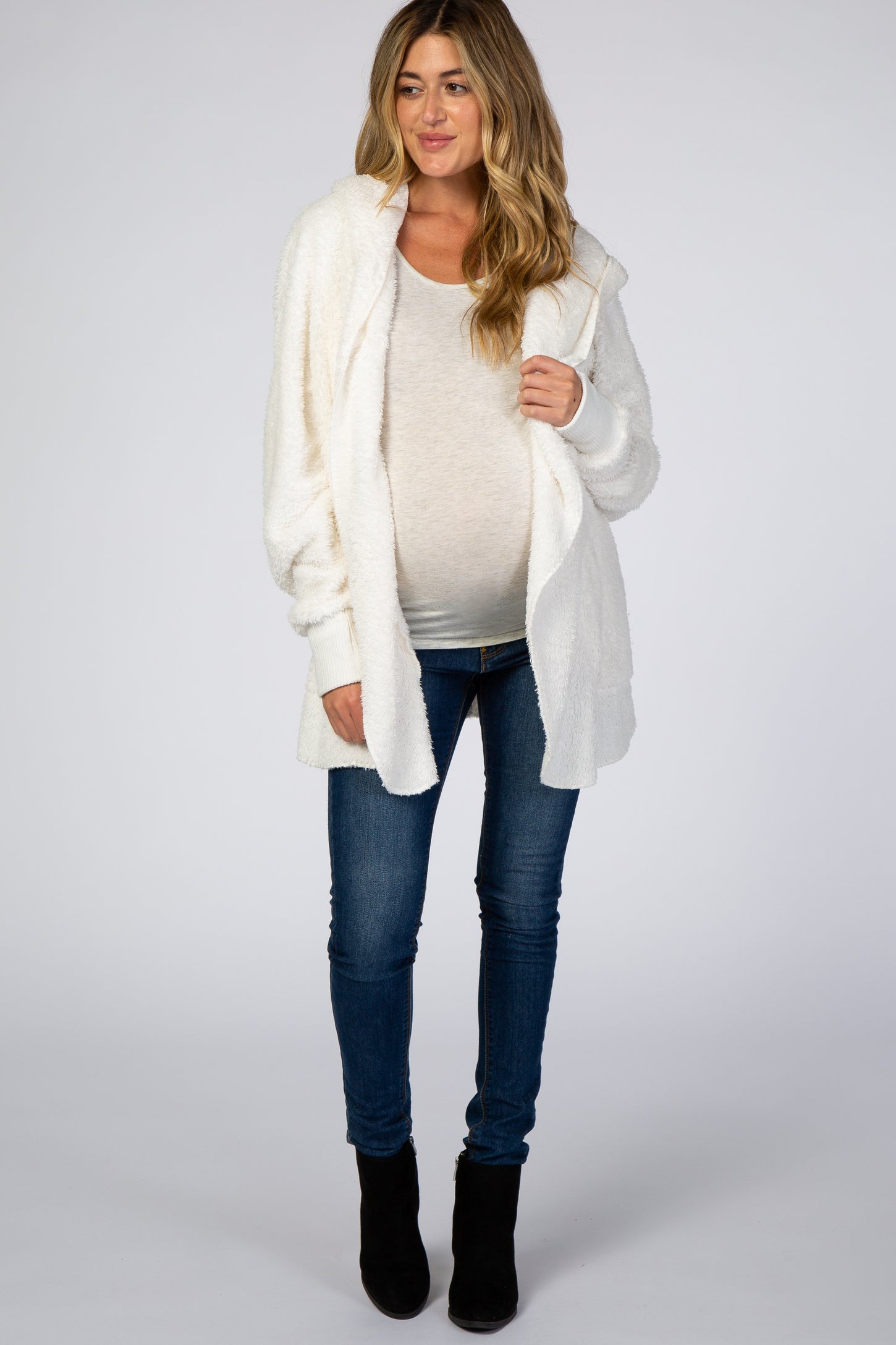 woman wearing a white maternity wear hooded cardigan over a light top and skinny jeans, with a visible baby bump