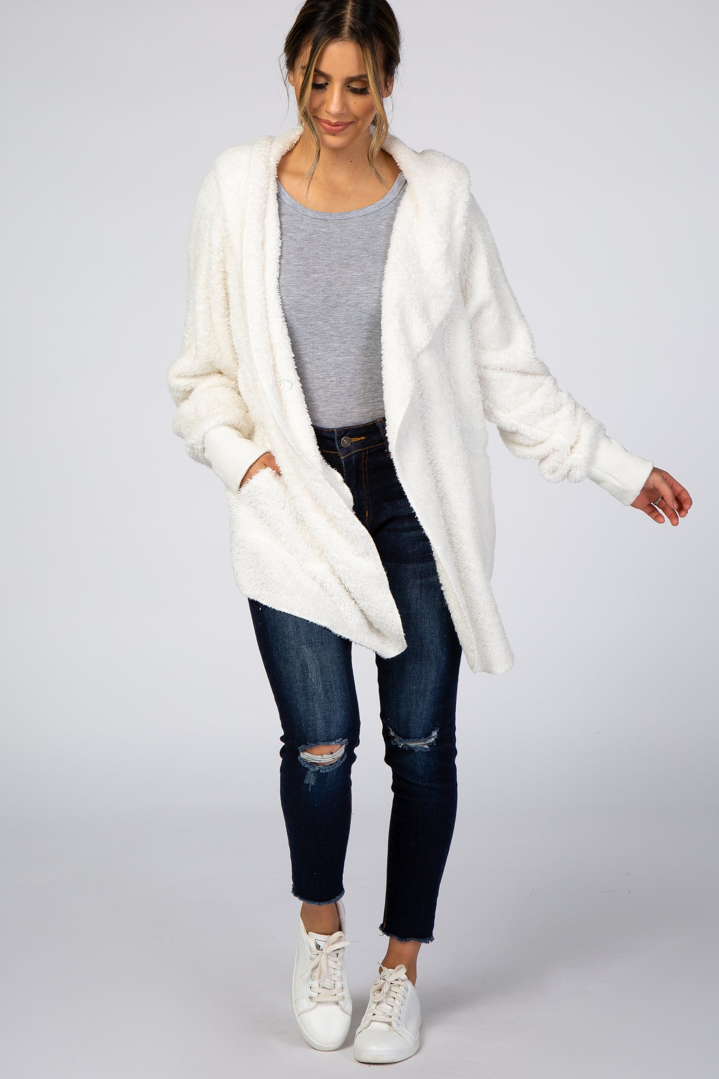 woman wearing a white cozy fuzzy cardigan over a gray top and ripped jeans, styled with white sneakers