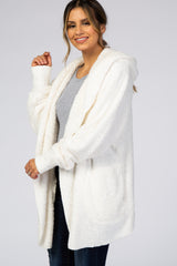 woman wearing a cozy white fleece hooded cardigan over a gray top, smiling and posing with one hand raised