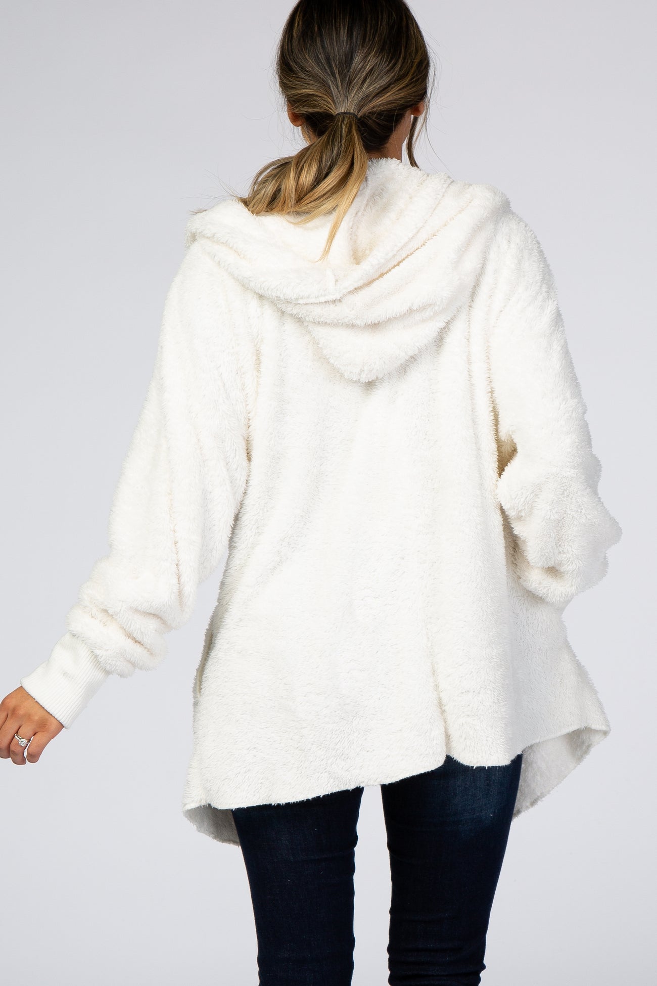 woman wearing a fluffy white hooded pullover sweater with a relaxed fit and deep hemline, seen from the back